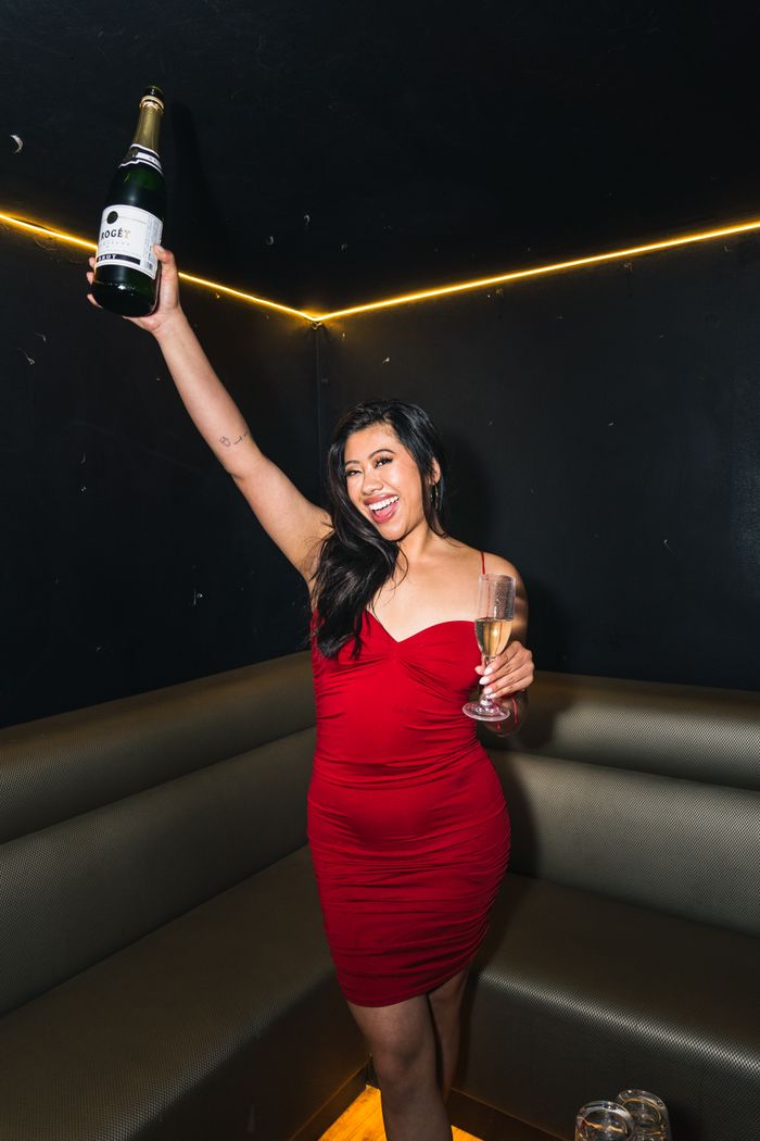 Woman in red dress joyfully holding champagne bottle in a festive indoor setting.