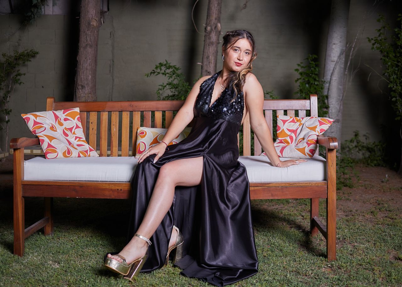 About Elegant woman in a black evening dress posing on a bench outdoors, showcasing fashion and style.