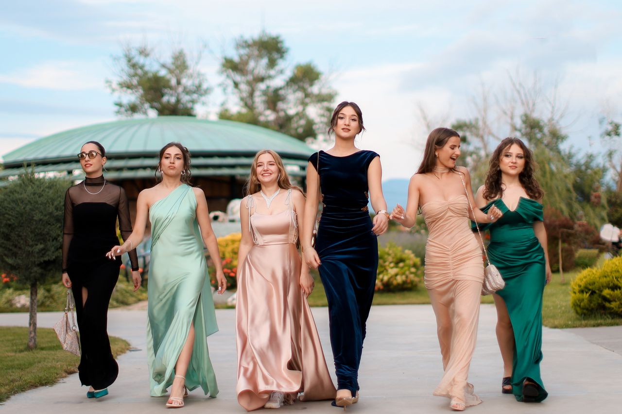 Services A group of six women in elegant evening dresses walking confidently outdoors, showcasing fashion and style.