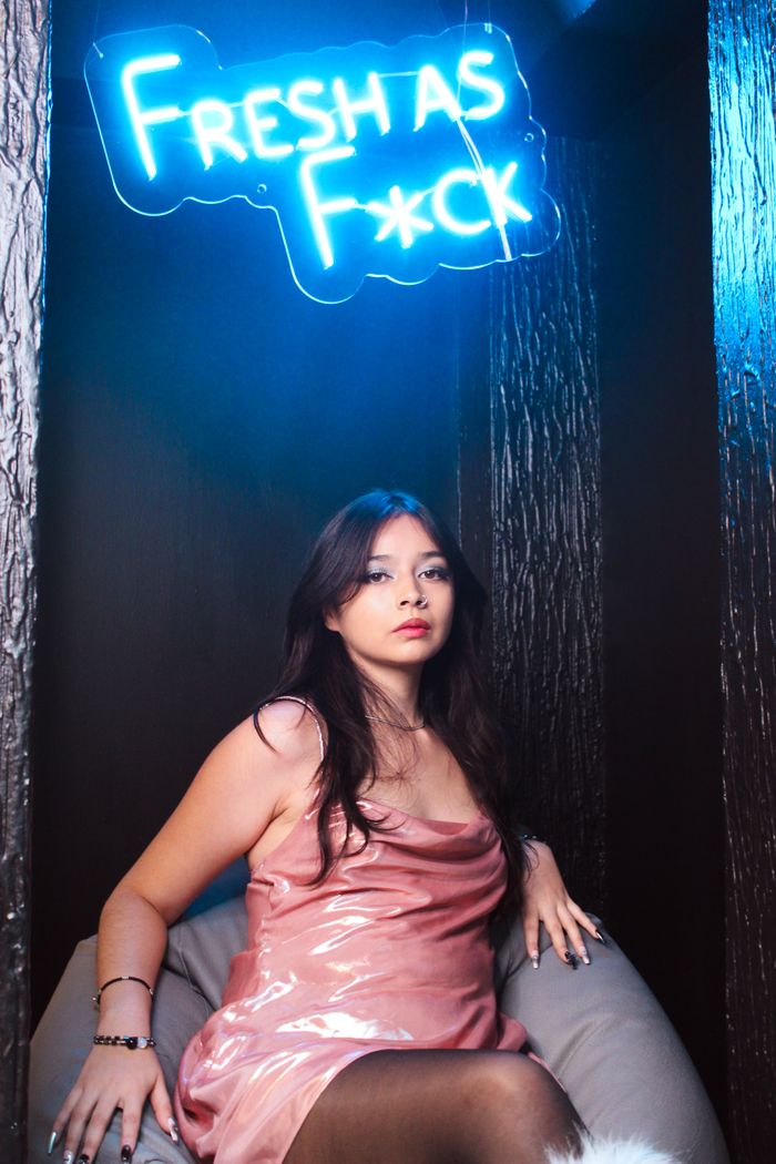 Services Young woman poses under neon light sign, showcasing modern fashion and attitude.