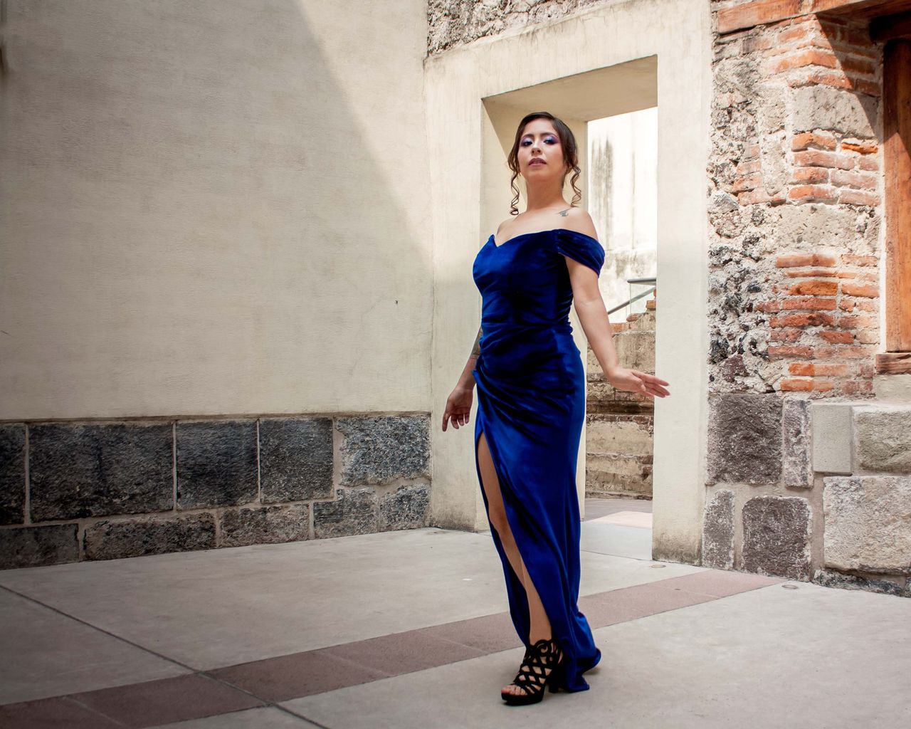 Services Graceful woman in a blue dress poses against rustic architecture, showcasing elegance and style.